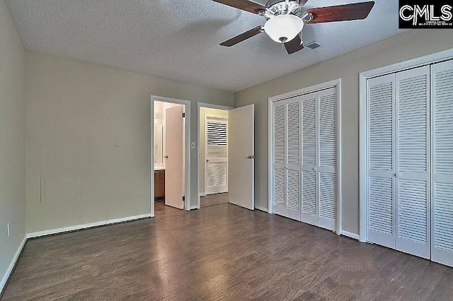 unfurnished bedroom with ceiling fan, dark hardwood / wood-style flooring, a textured ceiling, and multiple closets