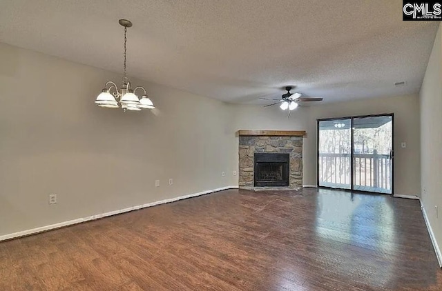 unfurnished living room featuring a textured ceiling, ceiling fan with notable chandelier, a stone fireplace, and dark wood-type flooring