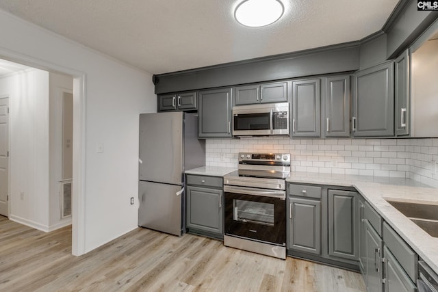 kitchen with gray cabinetry, light hardwood / wood-style flooring, a textured ceiling, decorative backsplash, and appliances with stainless steel finishes