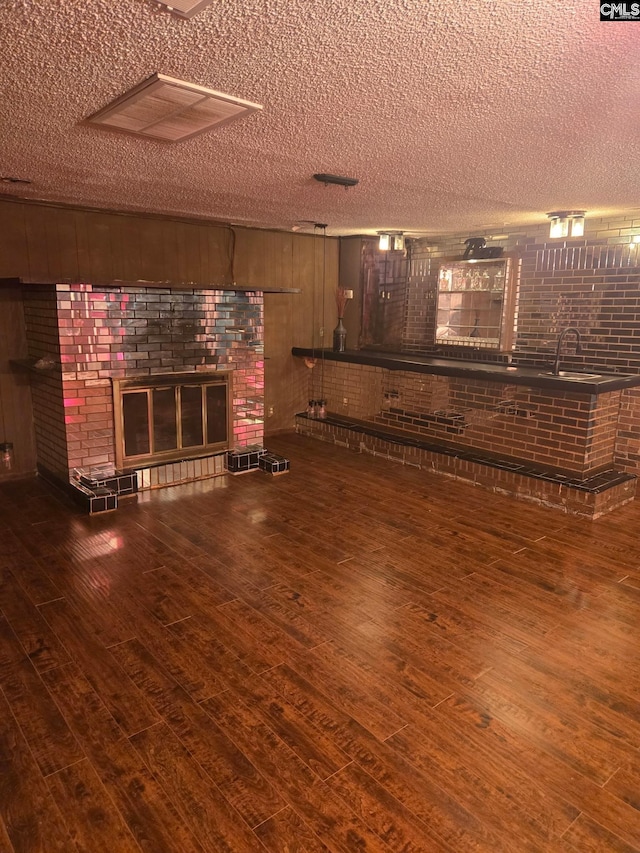 unfurnished living room with a fireplace, brick wall, dark hardwood / wood-style floors, and a textured ceiling