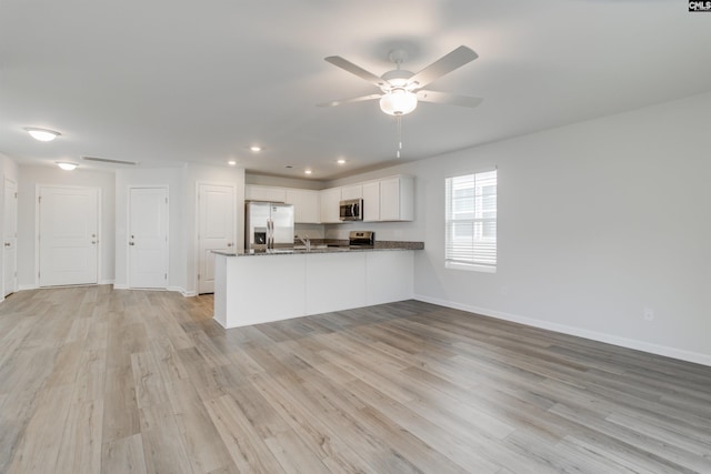 kitchen with stainless steel appliances, light hardwood / wood-style flooring, kitchen peninsula, dark stone counters, and white cabinets