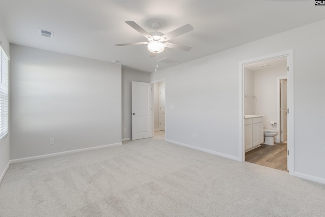 unfurnished bedroom featuring light carpet, multiple windows, ensuite bathroom, and ceiling fan