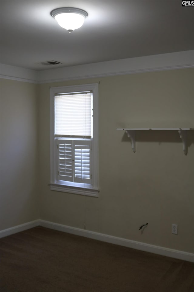 empty room with ornamental molding and dark colored carpet