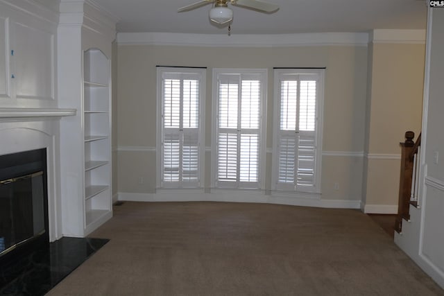 unfurnished living room featuring ceiling fan, built in shelves, crown molding, and dark colored carpet