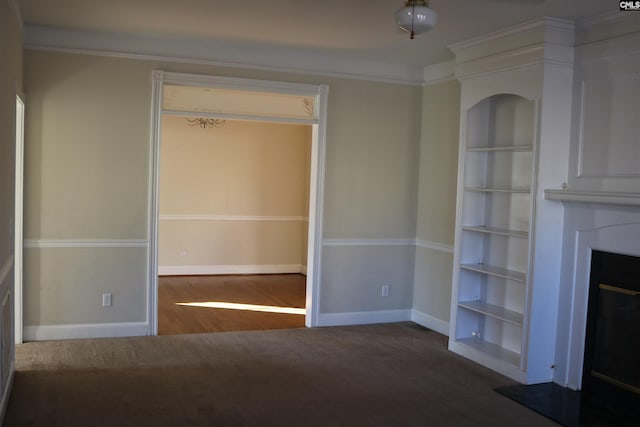 unfurnished living room featuring ornamental molding, built in shelves, and dark colored carpet