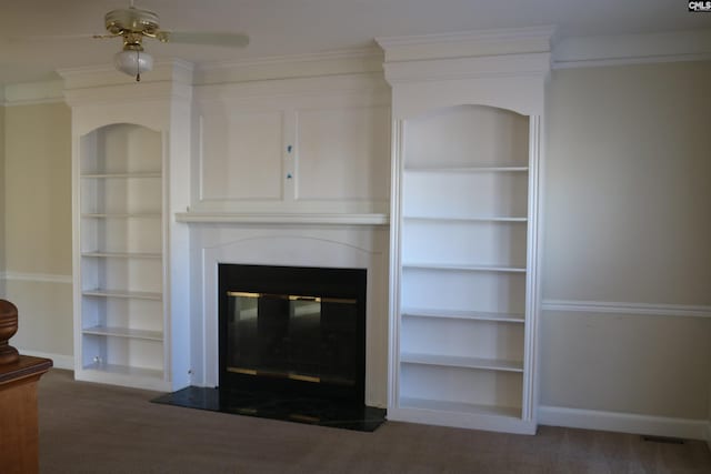 unfurnished living room featuring ceiling fan, crown molding, built in shelves, and dark carpet