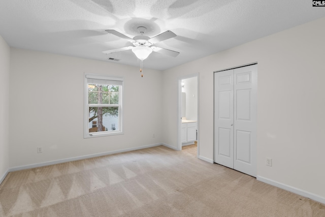 unfurnished bedroom with light carpet, ensuite bath, a textured ceiling, ceiling fan, and a closet