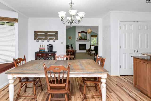 dining room with a chandelier, crown molding, light hardwood / wood-style flooring, and a brick fireplace