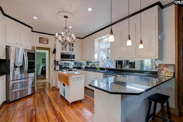 kitchen with appliances with stainless steel finishes, hardwood / wood-style flooring, white cabinets, a center island, and hanging light fixtures