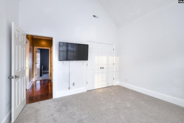 unfurnished bedroom featuring carpet, a closet, and high vaulted ceiling