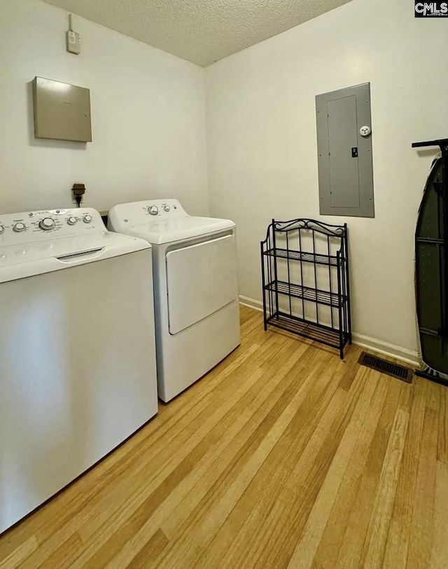 laundry area featuring electric panel, light hardwood / wood-style floors, a textured ceiling, and washing machine and clothes dryer