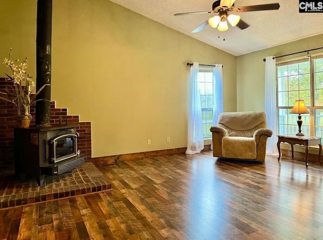 sitting room with a textured ceiling, vaulted ceiling, a wood stove, dark hardwood / wood-style flooring, and ceiling fan