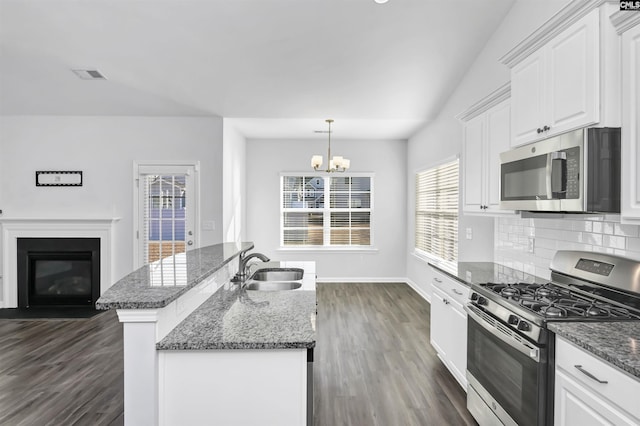 kitchen with hanging light fixtures, stainless steel appliances, an island with sink, backsplash, and white cabinets