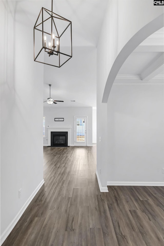 unfurnished living room with ceiling fan with notable chandelier and dark wood-type flooring