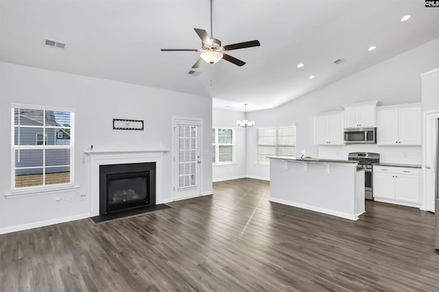 unfurnished living room featuring ceiling fan with notable chandelier, dark wood-type flooring, and vaulted ceiling