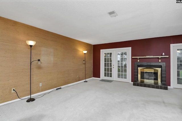 unfurnished living room featuring a fireplace, wood walls, french doors, and carpet floors