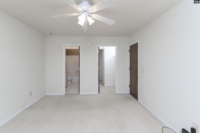 unfurnished bedroom with a closet, light colored carpet, ceiling fan, a spacious closet, and ensuite bathroom