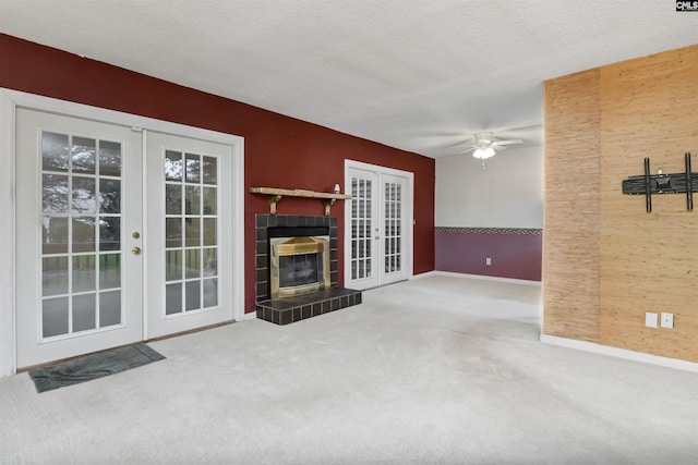 unfurnished living room featuring a tile fireplace, a textured ceiling, carpet, french doors, and ceiling fan