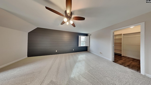 unfurnished bedroom with a closet, dark colored carpet, ceiling fan, a walk in closet, and lofted ceiling