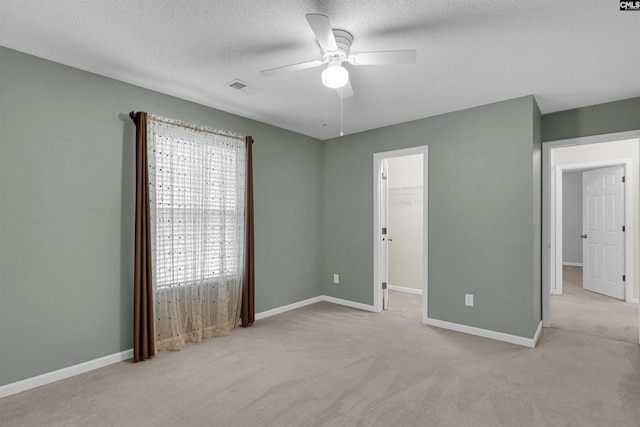 unfurnished bedroom with ceiling fan, light colored carpet, a spacious closet, and multiple windows