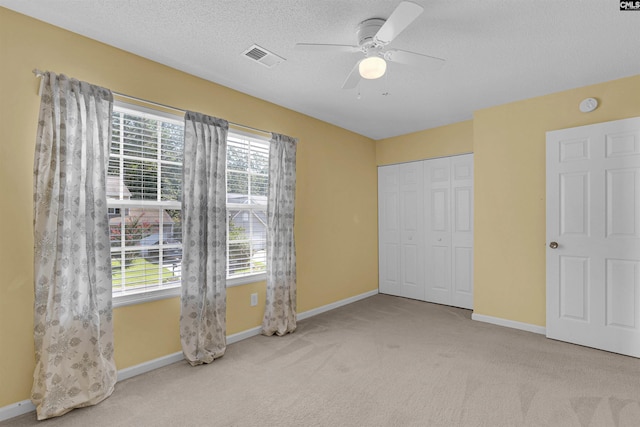 unfurnished bedroom featuring light carpet, a closet, ceiling fan, and a textured ceiling