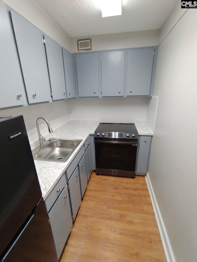 kitchen with stainless steel range with electric cooktop, sink, a textured ceiling, refrigerator, and light wood-type flooring