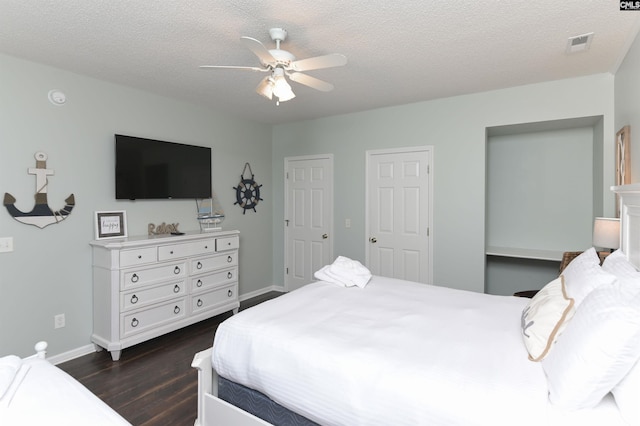 bedroom featuring dark wood-type flooring, a textured ceiling, ceiling fan, and multiple closets