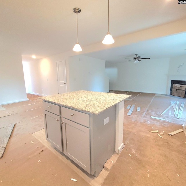 kitchen featuring light stone counters, a ceiling fan, decorative light fixtures, open floor plan, and a center island