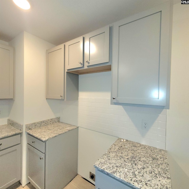 kitchen with decorative backsplash, light stone counters, and gray cabinets