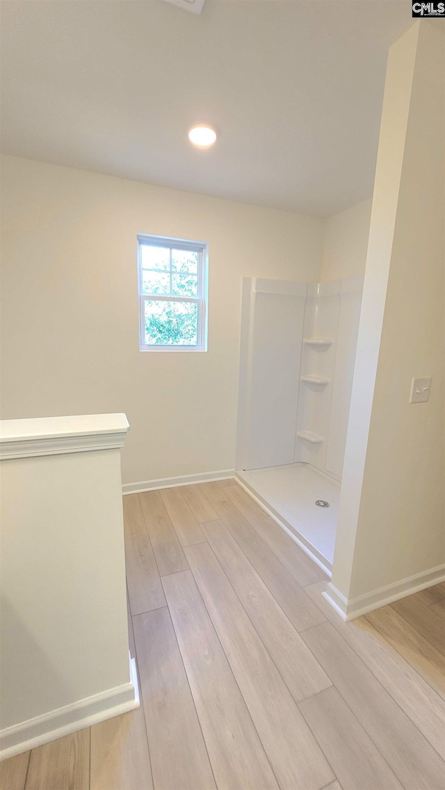 bathroom with wood finished floors, baseboards, and walk in shower