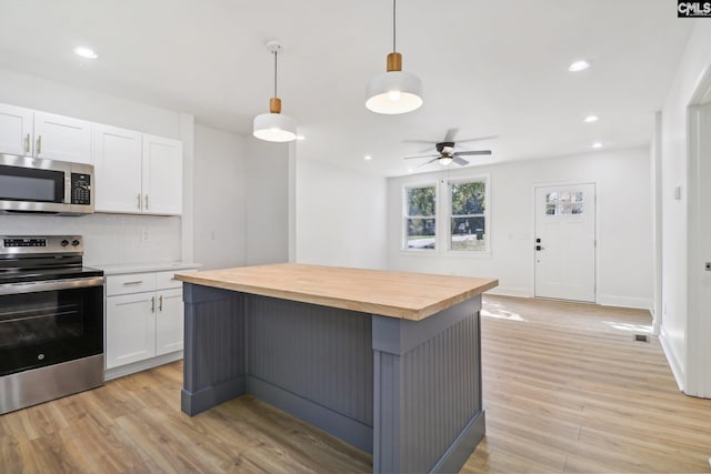 kitchen with appliances with stainless steel finishes, ceiling fan, pendant lighting, butcher block countertops, and white cabinets