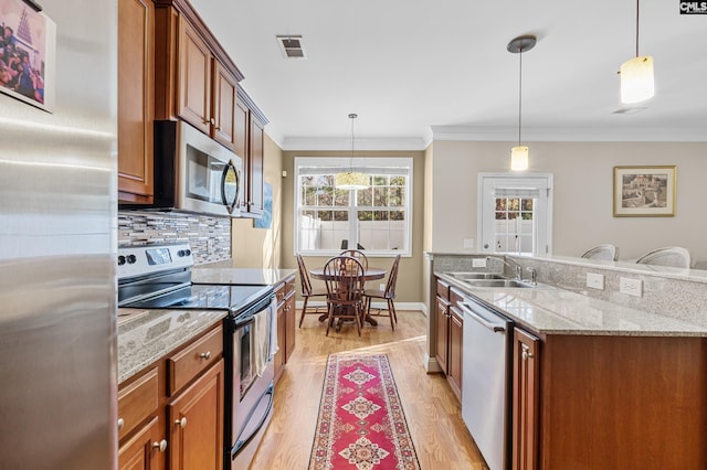 kitchen featuring stainless steel appliances, decorative light fixtures, ornamental molding, and light hardwood / wood-style flooring