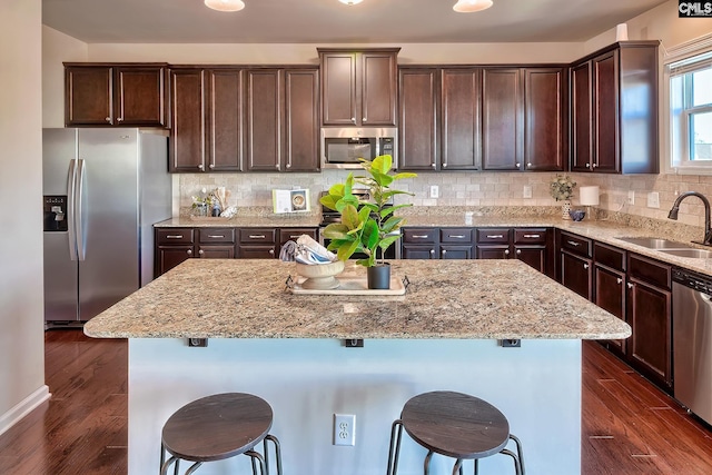 kitchen with light stone countertops, a kitchen bar, dark wood-type flooring, and appliances with stainless steel finishes