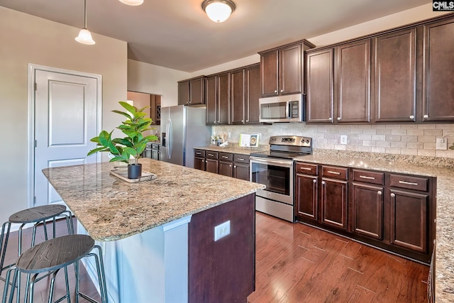 kitchen featuring appliances with stainless steel finishes, hanging light fixtures, light stone counters, and backsplash