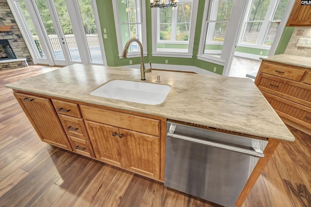 kitchen featuring dishwasher, a stone fireplace, a center island with sink, a notable chandelier, and sink