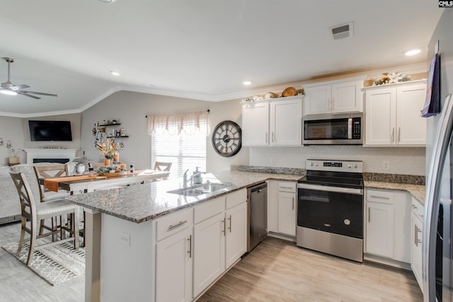 kitchen with kitchen peninsula, appliances with stainless steel finishes, white cabinets, and sink