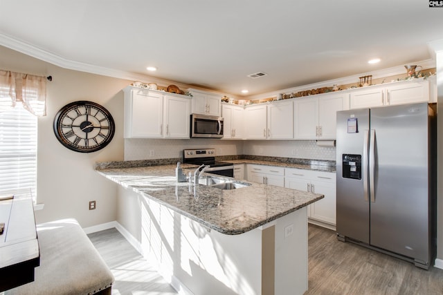 kitchen featuring dark stone countertops, stainless steel appliances, crown molding, white cabinets, and light hardwood / wood-style flooring