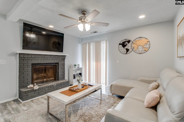 living room featuring a textured ceiling, a fireplace, ceiling fan, and light hardwood / wood-style floors