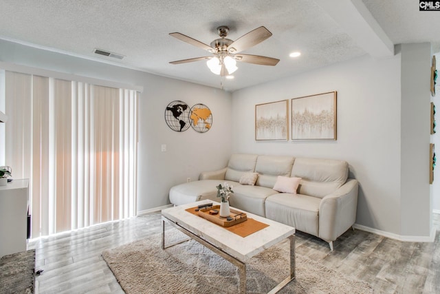 living room with a textured ceiling, ceiling fan, light hardwood / wood-style flooring, and beamed ceiling