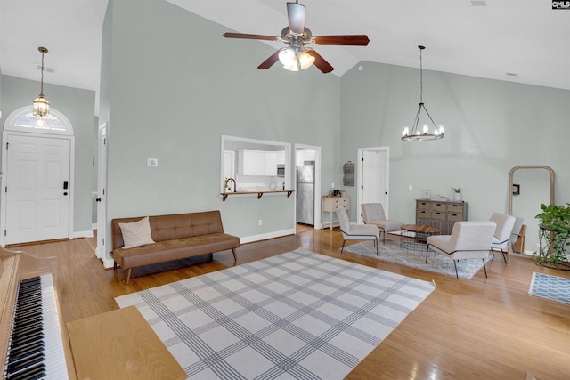 living room featuring ceiling fan with notable chandelier, high vaulted ceiling, light hardwood / wood-style floors, and sink