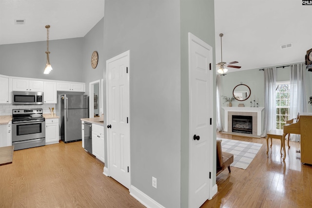 kitchen with stainless steel appliances, high vaulted ceiling, backsplash, white cabinets, and ceiling fan