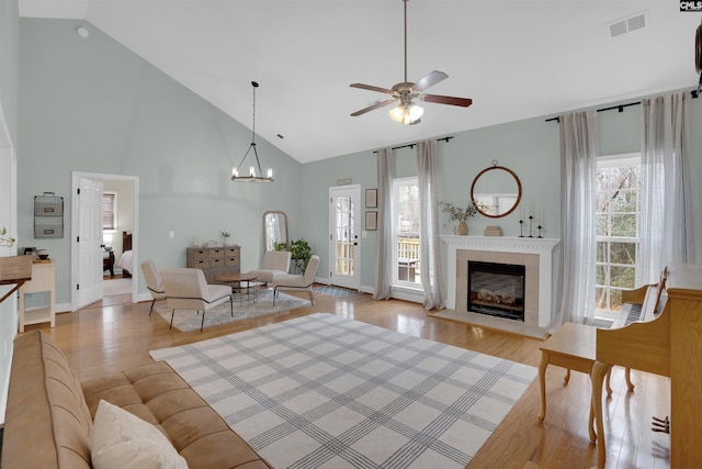 living room featuring ceiling fan with notable chandelier, high vaulted ceiling, and light hardwood / wood-style flooring