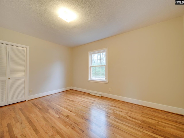 unfurnished bedroom featuring a closet, a textured ceiling, and light hardwood / wood-style flooring