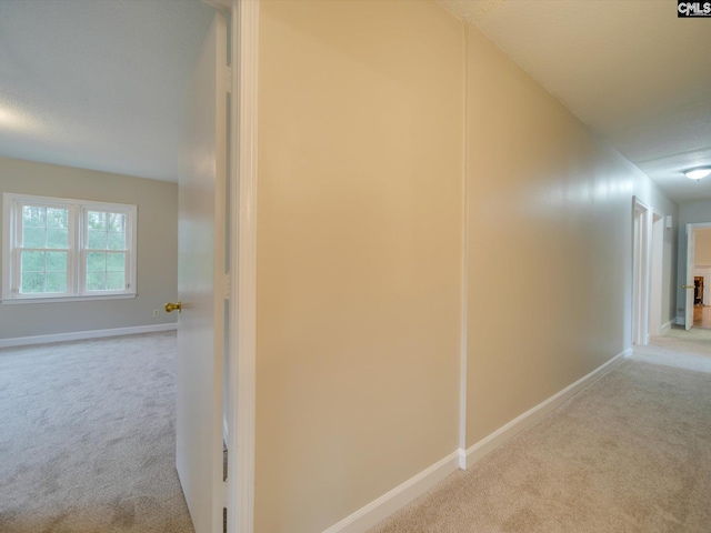 hallway with a textured ceiling and light carpet