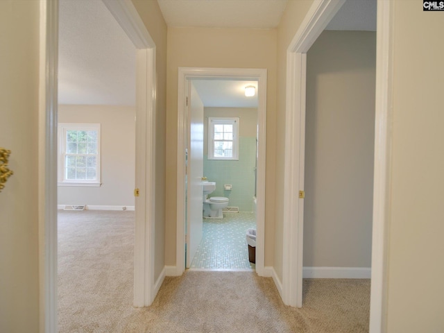 hall with tile walls and light carpet