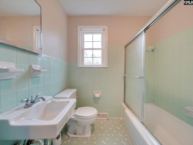 full bathroom featuring toilet, combined bath / shower with glass door, tile patterned floors, tile walls, and sink