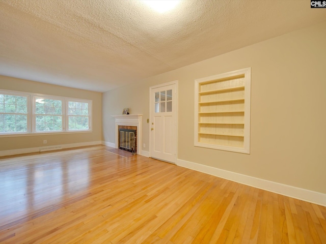 unfurnished living room featuring a textured ceiling, built in features, and light hardwood / wood-style flooring