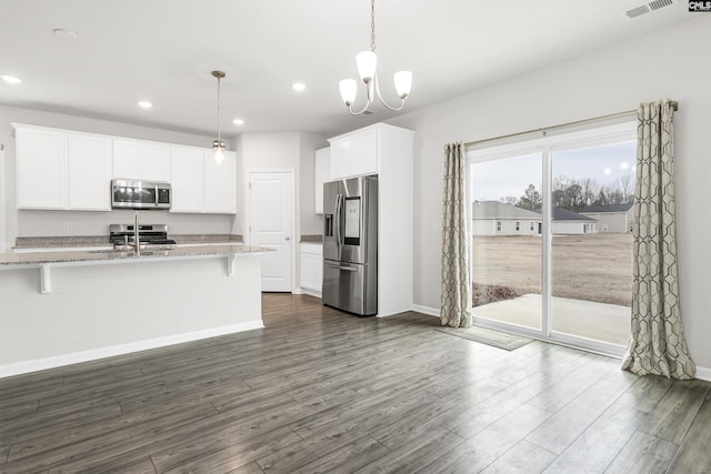 kitchen with decorative light fixtures, white cabinets, a kitchen bar, light stone countertops, and appliances with stainless steel finishes