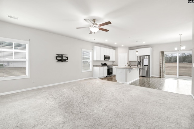 kitchen featuring pendant lighting, stainless steel appliances, a center island with sink, ceiling fan with notable chandelier, and white cabinets