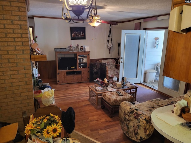 living room featuring wooden walls, a textured ceiling, hardwood / wood-style flooring, and crown molding